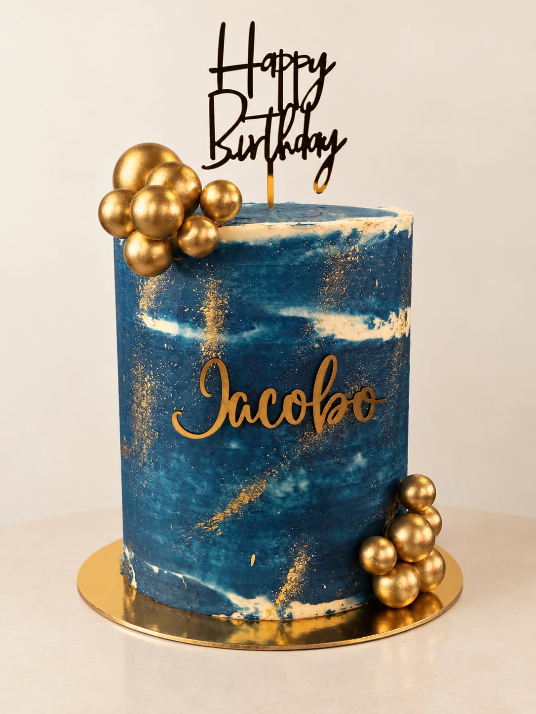 Torta alta azul con pinceladas doradas, esferas y el nombre Jacobo.