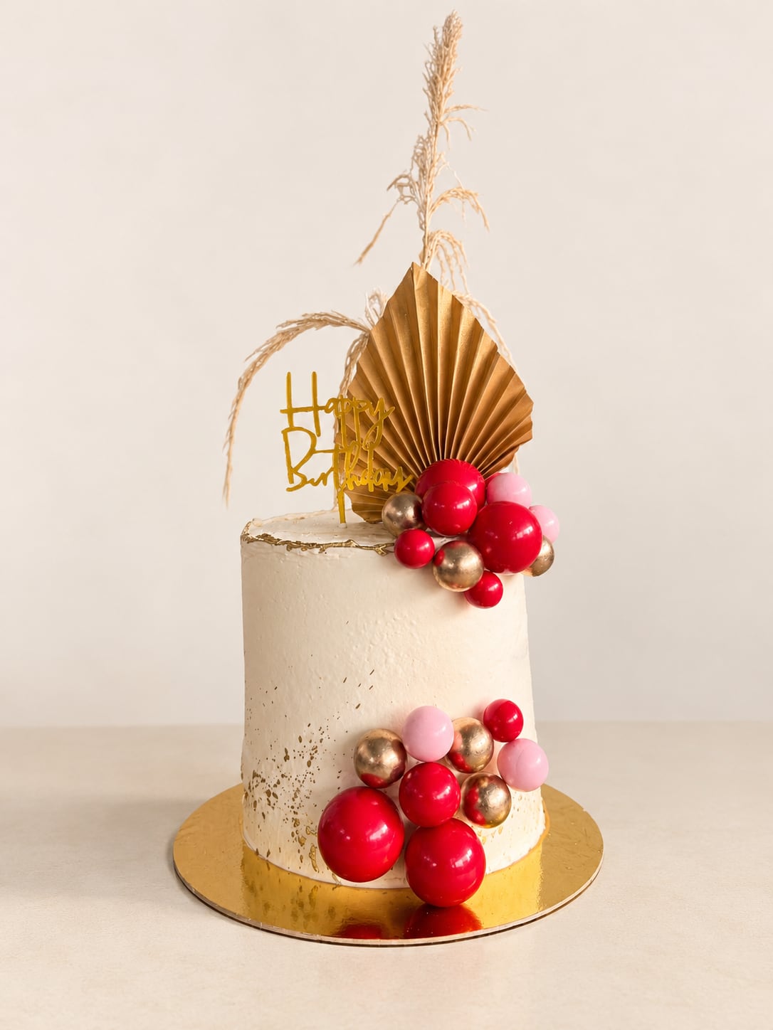 Torta blanca con esferas rojas, rosas y doradas y un abanico decorativo.