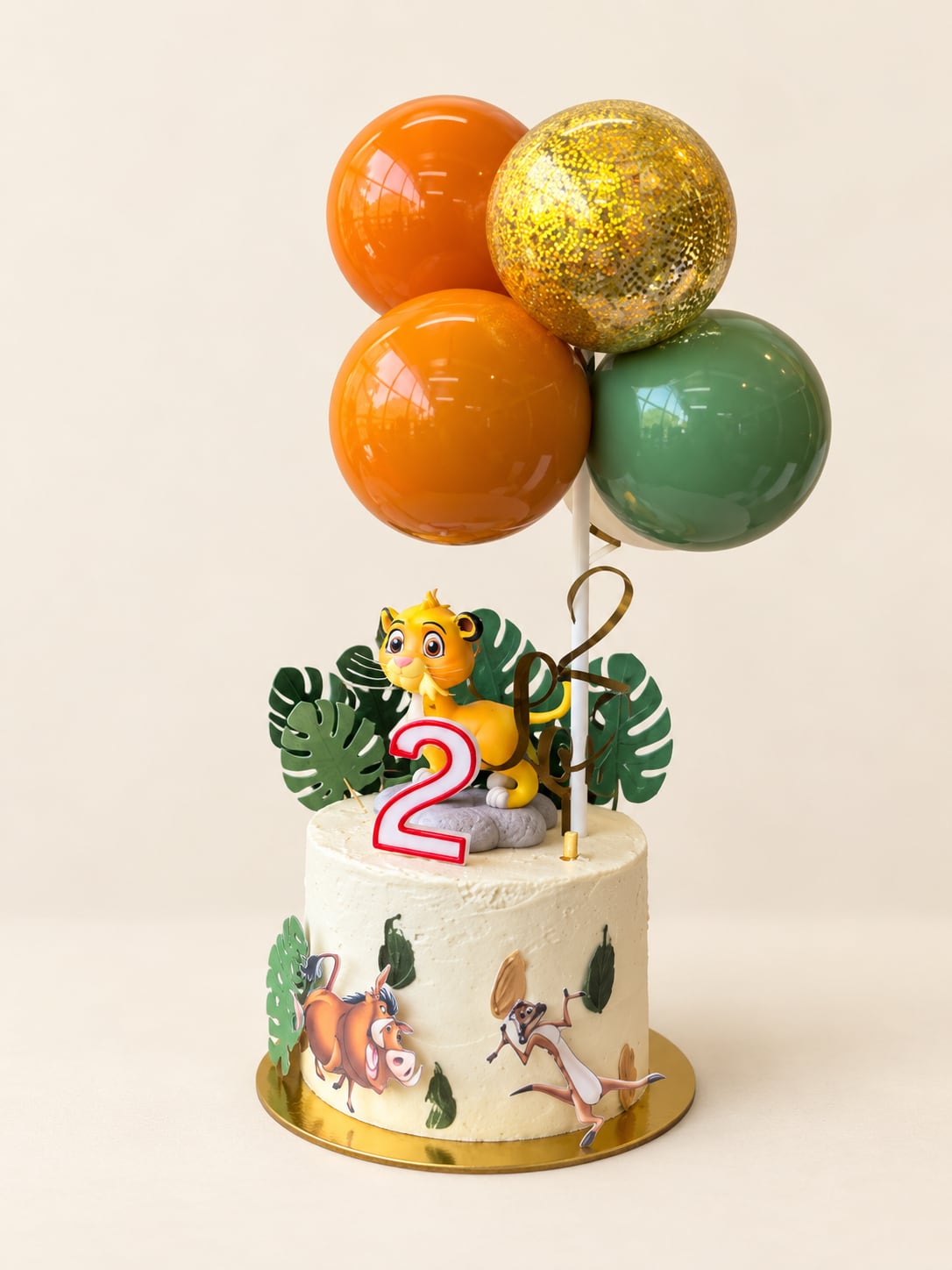 Torta blanca de El Rey León con Simba, vela de dos años, hojas verdes y globos naranjas, verde y dorado.